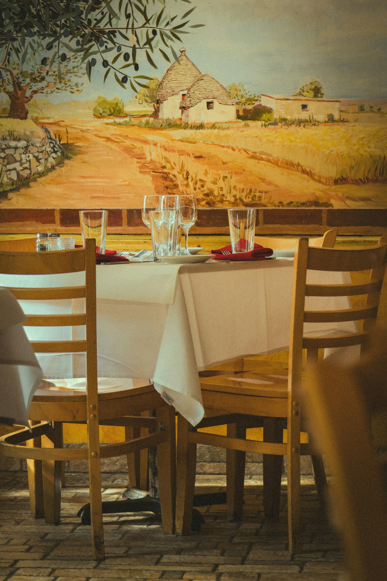 Gedeckter Tisch in der Osteria mit Holzstühlen vor einem gemalten Landschaftsbild