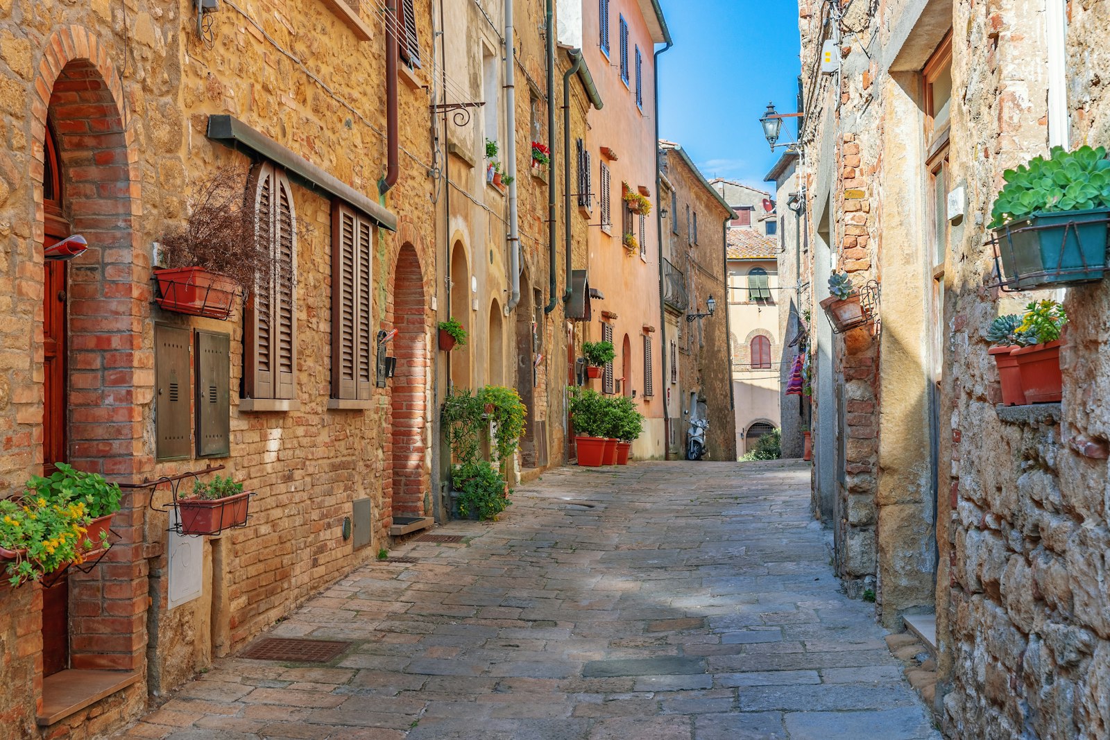 Enge Altstadtgasse aus warmem Sandstein mit Fensterläden und Blumentöpfen