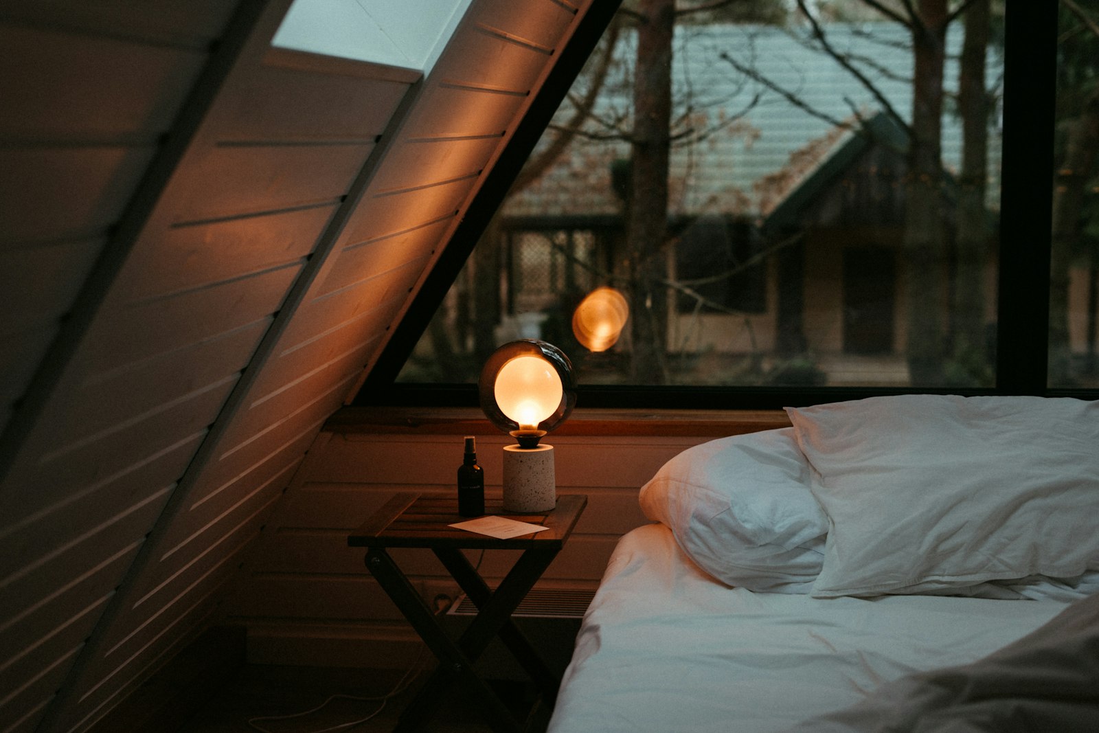 Zimmer unter der Dachschräge mit Bett, Nachttisch und warmer Leselampe