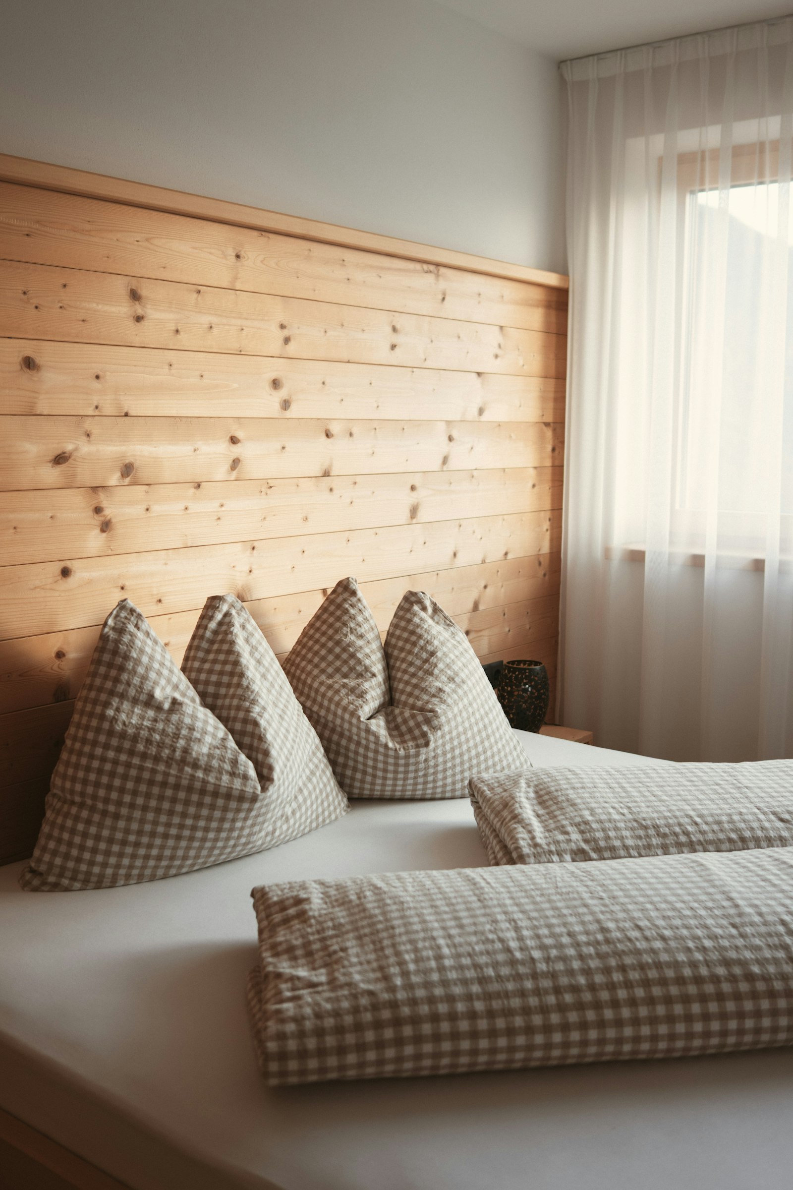 Bett vor getäfelter Holzwand im Zimmer Wiesenblick, Fenster mit Vorhang im Hintergrund