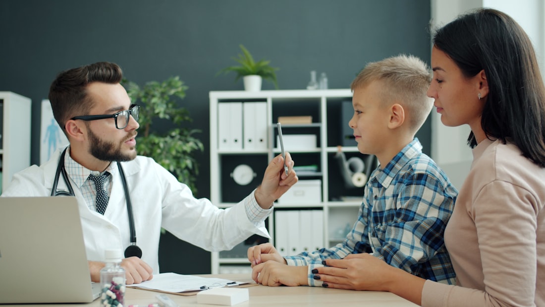 Kinderarzt im Gespräch mit einem Jungen und seiner Mutter im Sprechzimmer