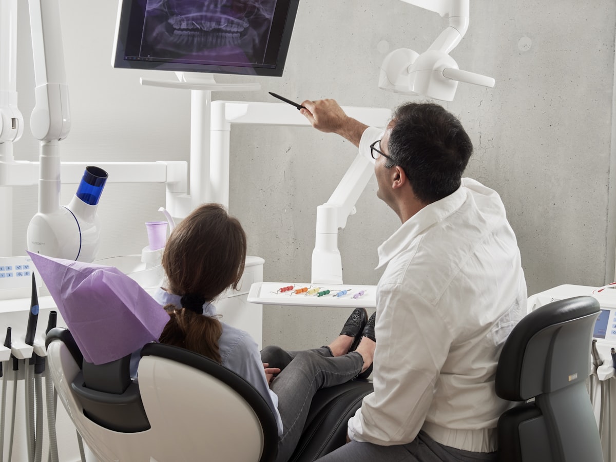 Zahnarzt erklärt einer Patientin ein digitales Röntgenbild am Monitor
