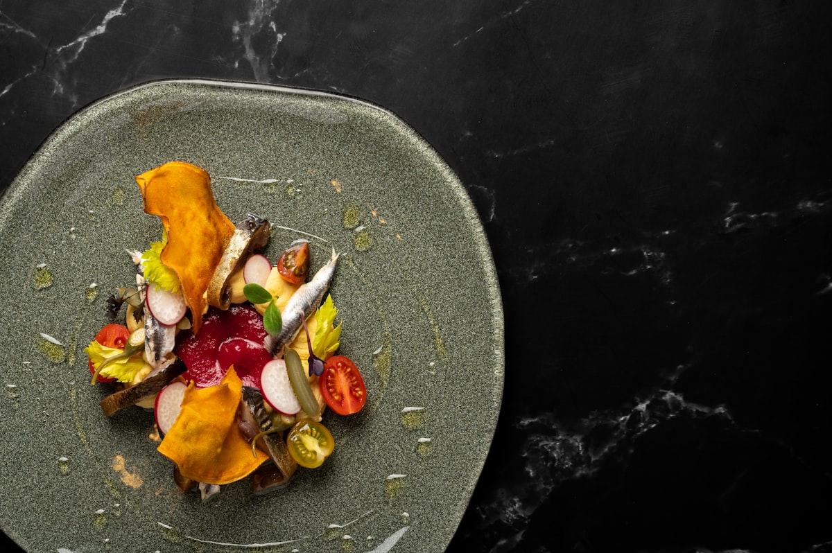 Sardinenfilets mit Radieschen, Kirschtomaten und Rote-Bete-Creme auf steingrauem Teller