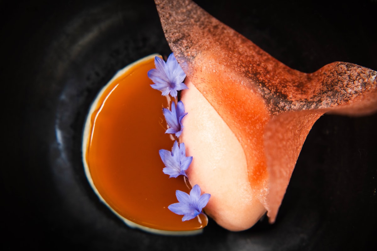 Aprikosensorbet mit Karamellsauce, Veilchenblüten und Knusperblatt auf dunklem Teller